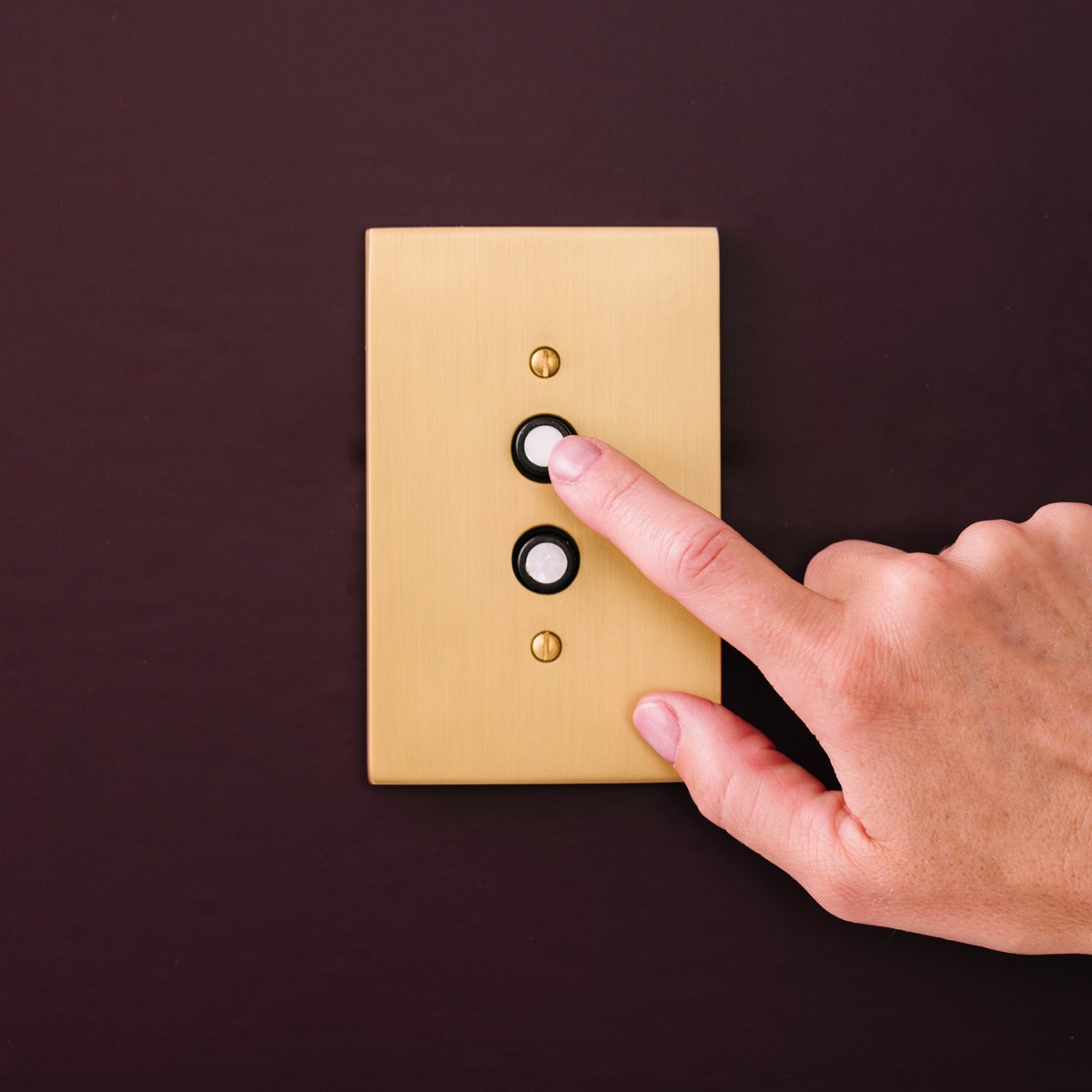 Vintage-style push-button light switch in polished brass finish mounted on wall